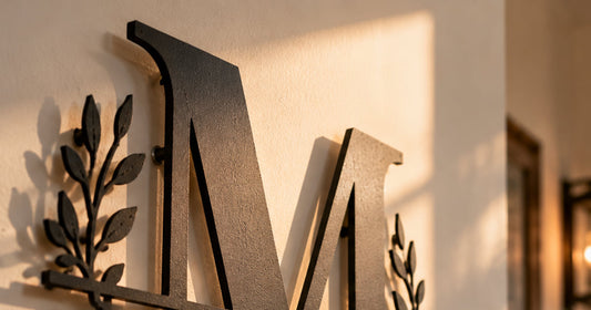 Close up of a black split letter monogram steel sign with foliage detail mounted on a warm white exterior wall